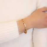 Female model wearing the Adored gold stainless steel bracelet, hand resting on opposite arm to display detailed crystal design and elegant gold shine.