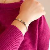 Female model wearing Alchemist bracelet highlighting polished steel and gold links, hand resting on opposite arm.