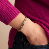 Female model wearing Alchemist bracelet with polished X-shaped links and polished gold spacers, hand in pocket.