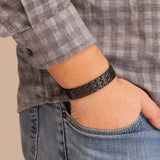 Man wearing the Brilliant Black matte stainless steel bracelet with thumb in pocket, showing understated checkered pattern.
