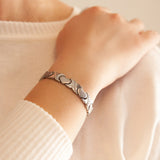 Female model wearing Love bracelet with heart and X link pattern, hand resting gently on opposite shoulder.