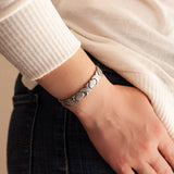 Love stainless steel bracelet on wrist with hand relaxed at side, showing alternating matte heart and polished X links.