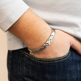 Male model wearing Maverick bracelet with curved puzzle-style interlocking links, matte centers, and polished edges, hand in pocket.