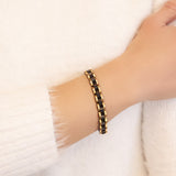 Model wearing the Perfect Balance black and gold stainless steel bracelet, hand resting on opposite arm to highlight matte black links and polished gold borders.