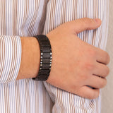 Male model resting hand on opposite arm while wearing Precious Black titanium bracelet, highlighting its geometric link design and triple embedded elements.