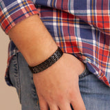 Man wearing the Pristine Black polished stainless steel bracelet with thumb in pocket, showing reflective engraved design.
