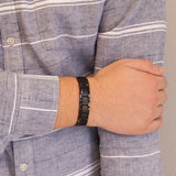 Male model wearing the Pure Black matte stainless steel bracelet, hand resting on opposite arm to display matte finish and refined black-steel contrast.