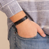 Man wearing the Pure Black matte stainless steel bracelet with thumb in pocket, showing polished borders and angular link design.