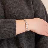 Female model wearing Serenity bracelet highlighting polished and matte alternating links with embedded elements, hand resting on opposite arm.
