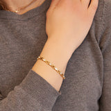 Female model wearing the Sparkle gold titanium bracelet, hand resting on opposite shoulder to display elegant crystal accents and golden luster.