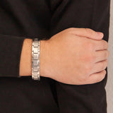 Male model wearing the Brilliant Balance stainless steel bracelet, hand resting on opposite arm to display refined angular link design and modern matte finish.