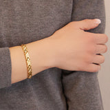 Female model wearing the Glistening Star gold titanium bracelet, hand resting on opposite arm to display elegant gold X-link design.